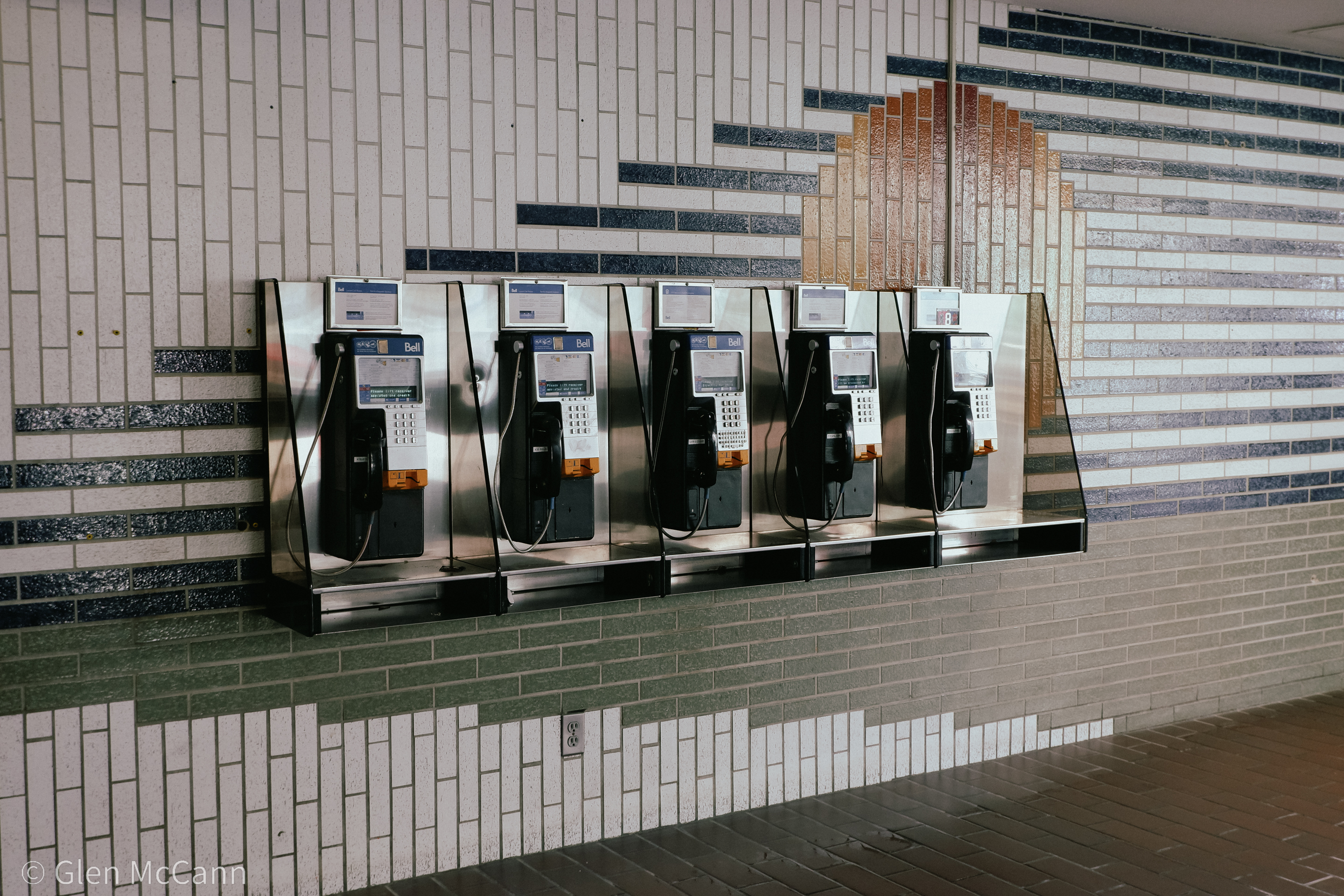 Photo of a line of pay phones against a colourful brick wall (indoors).