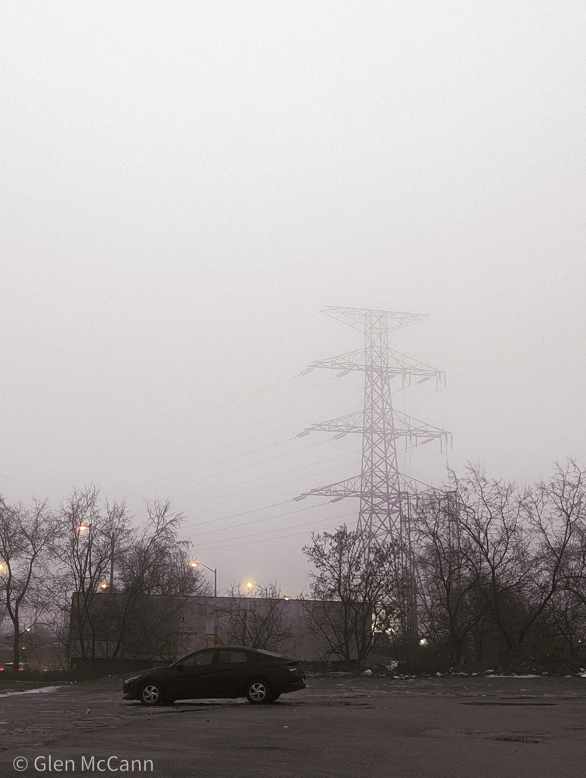 Photo of a car in a foggy parking lot with a radio tower in the background.