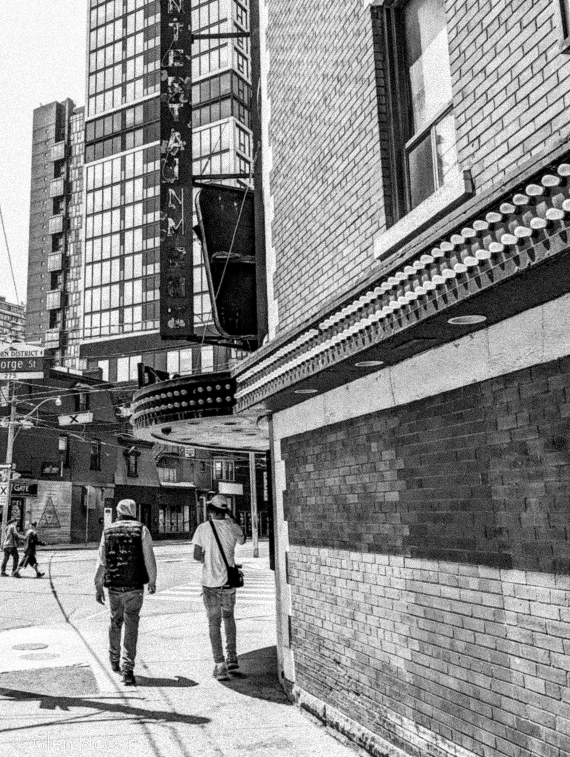 Black and white photo of two men walking past Filmore's in Toronto, shot from behind.