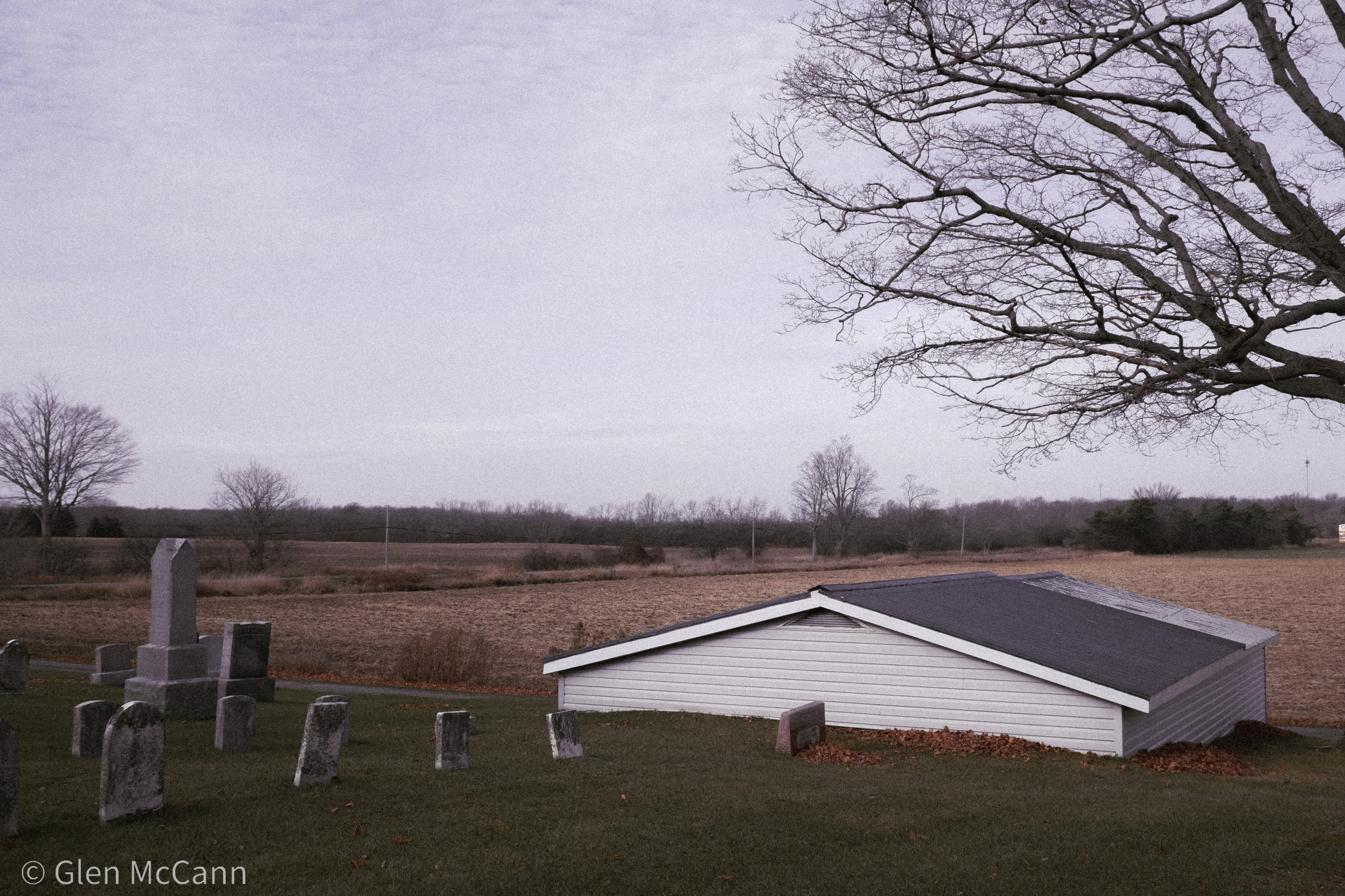 Photo of a house that is sunken into a hill in a cemetery next to an empty field.