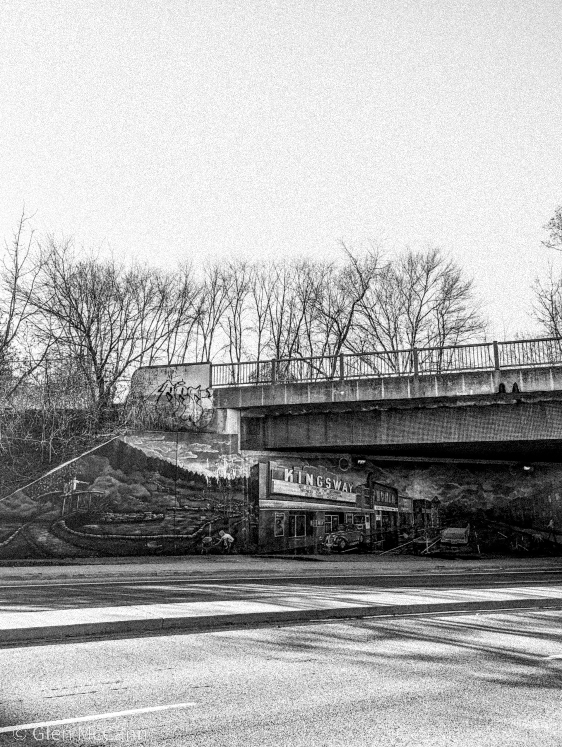 Black and white photo of a bridge in Toronto with a mural depicting Kingsway Cinemas underneath.
