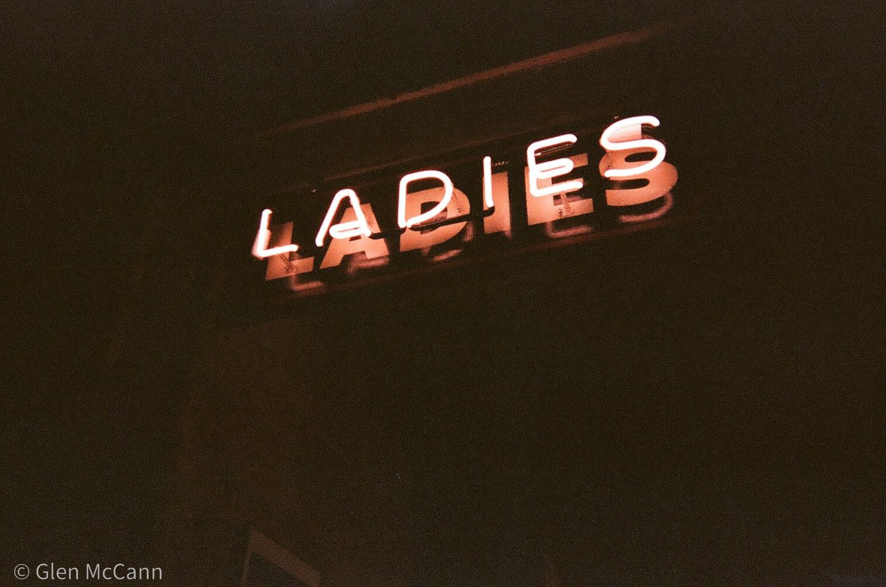 Film photo of a neon bathroom sign reading 'LADIES', the rest of the photo is too dark to make out.